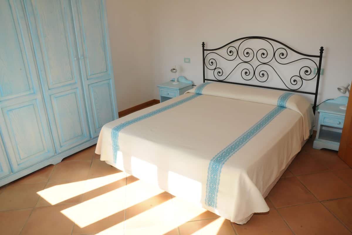 Una cama bien hecha con un cabecero decorativo, una mesita de noche con lámpara y un armario con detalles en azul claro.