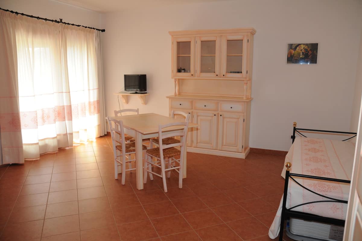Una habitación con una mesa de comedor, sillas, un televisor, un armario y una cama.