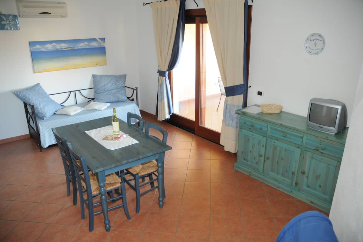 Una habitación con una cama, una mesa con sillas, un televisor sobre un mueble y un cuadro en la pared.