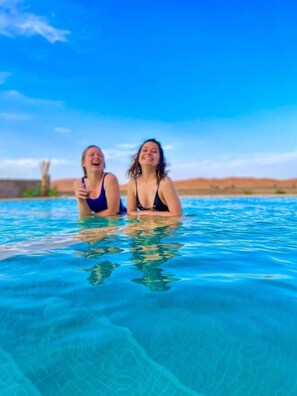 Zwei Personen in einem klaren, blauen Pool mit einer Wüstenlandschaft im Hintergrund.