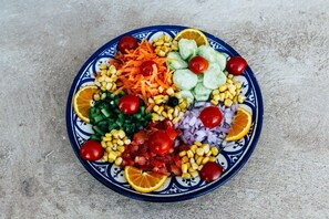 A plate of mixed vegetables and fruits on a textured surface. - Riad Caravasar (Taouz)