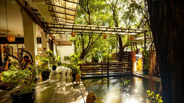 Un jardín interior tranquilo con un pequeño estanque, plantas en macetas y un puente de madera.
