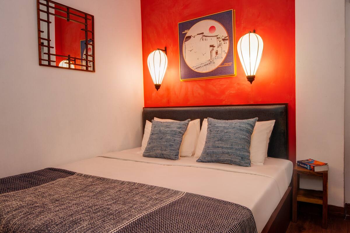 A hotel room with a bed, pillows, a bedside table, and wall art.
