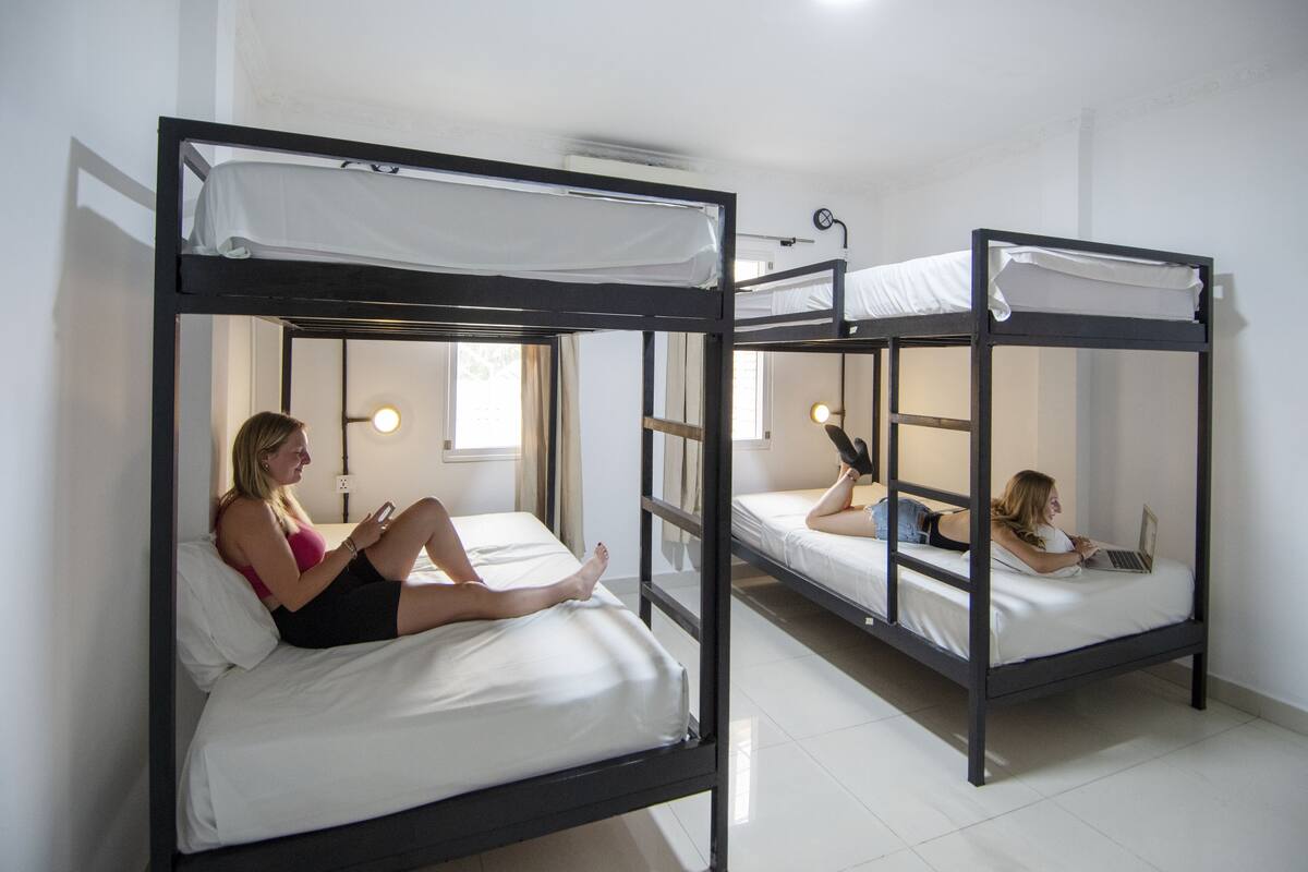 A dormitory room with bunk beds, a window, and a lamp.