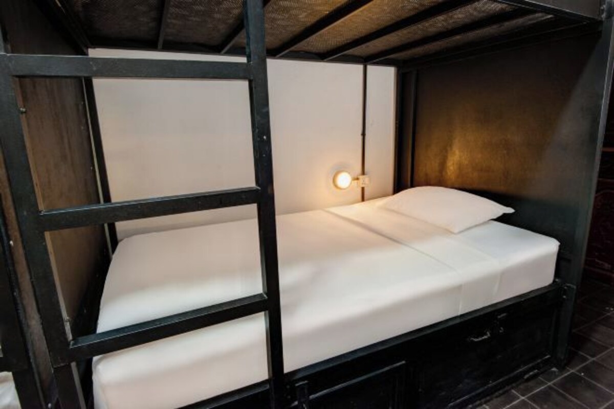 A bunk bed with a white mattress and pillows, a small bedside table, and a wall-mounted light.