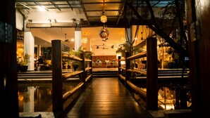 Un puente de madera que conduce a un restaurante con luces colgantes y vistas del interior.