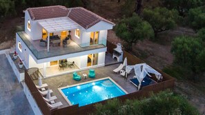 A two-story house with a swimming pool, outdoor seating, and a patio area.