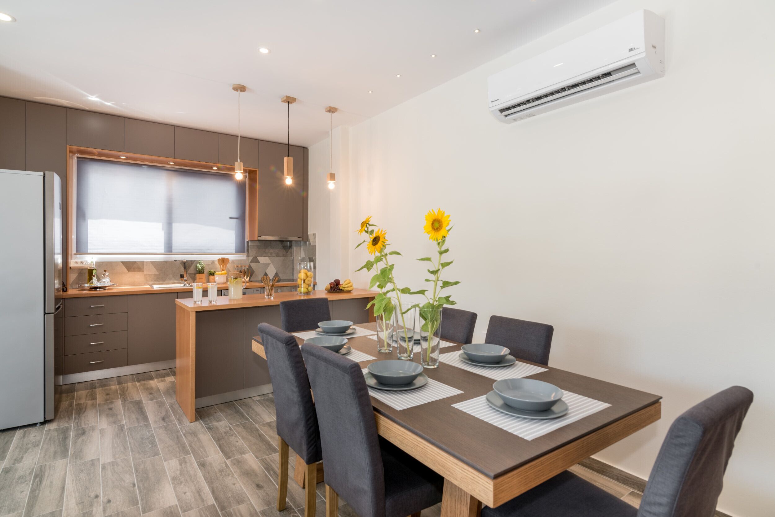 Een moderne keuken met een centraal eiland, een eethoek met een houten tafel en grijze stoelen, en een inbouwoven.