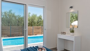 Une chambre avec une porte-fenêtre coulissante donnant sur une piscine, un bureau blanc et un miroir au mur.