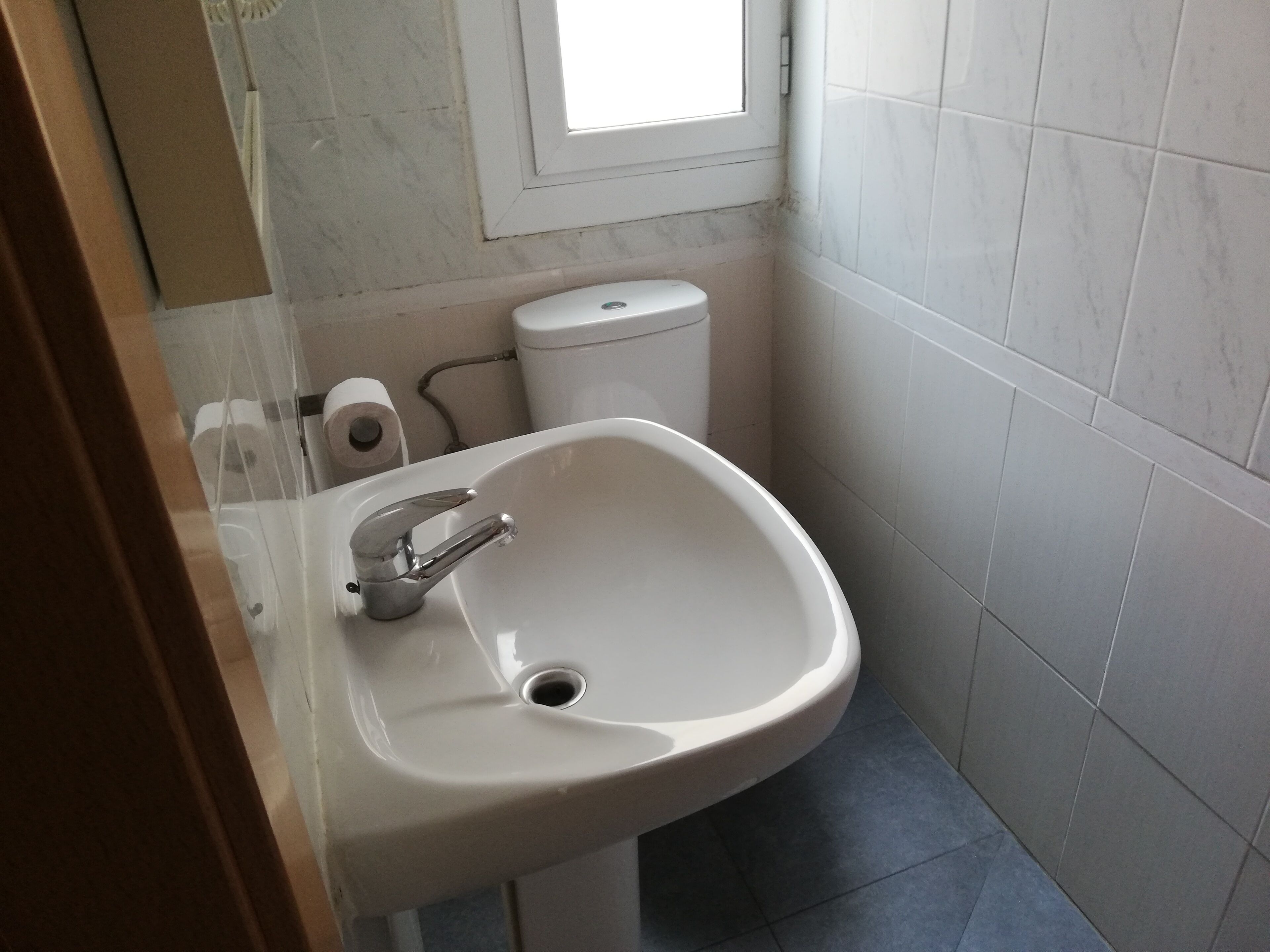 Une salle de bain avec un lavabo blanc, des toilettes et une fenêtre.