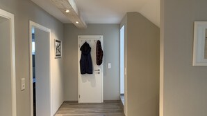 Um corredor com teto de madeira, uma porta branca e um casaco pendurado nela, além de um quadro na parede.
