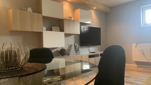 Uma sala de estar moderna com uma mesa de jantar de vidro, cadeiras pretas, uma televisão de tela plana na parede e estantes embutidas.