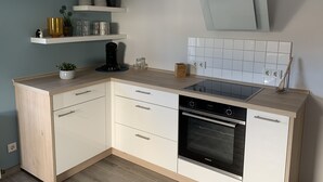 Uma cozinha moderna com armários brancos, forno embutido e bancada com cafeteira e copos.
