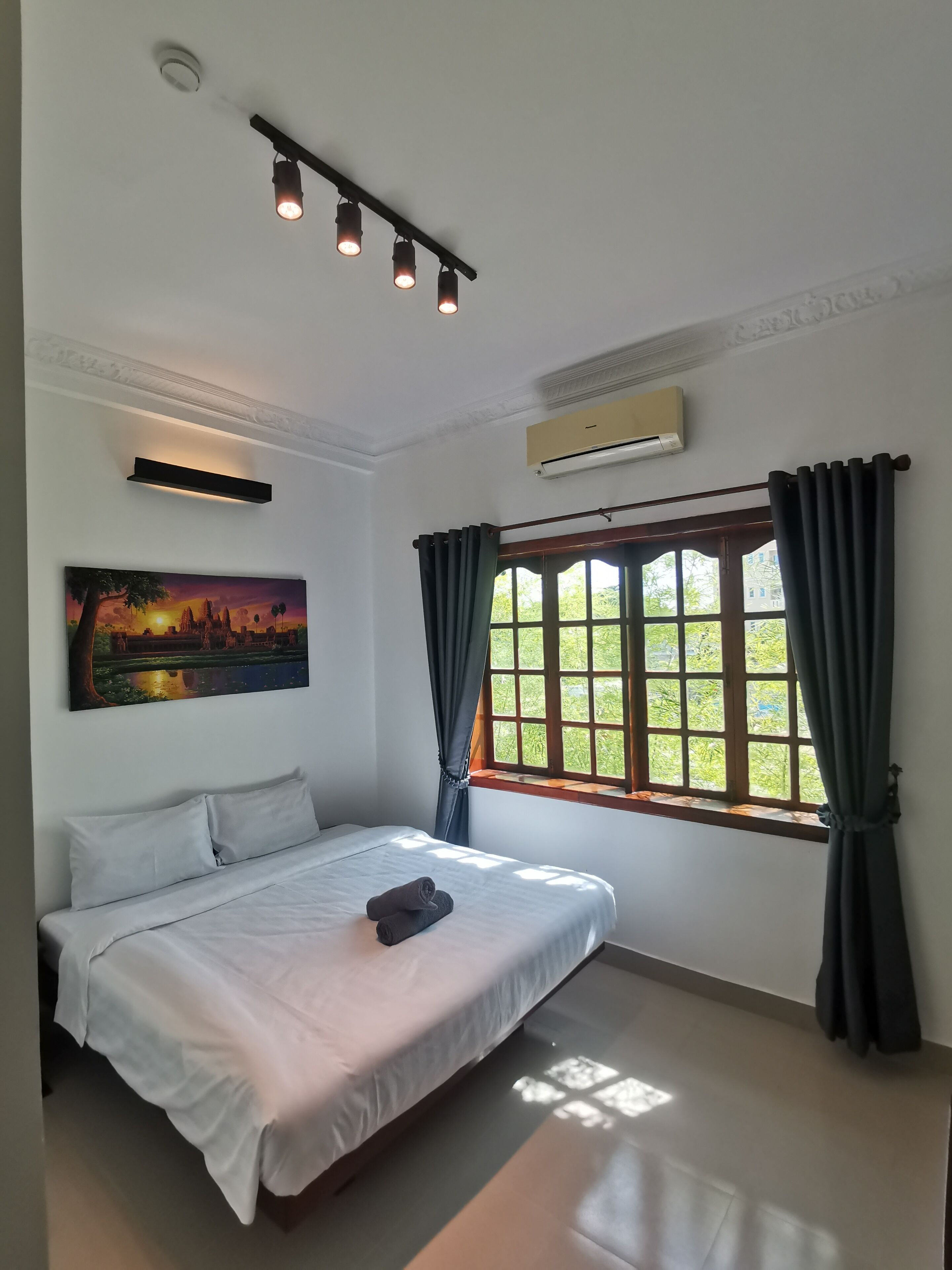 Ein Schlafzimmer mit Bett, einem Gemälde, einem Fenster mit Vorhängen und einer Klimaanlage.