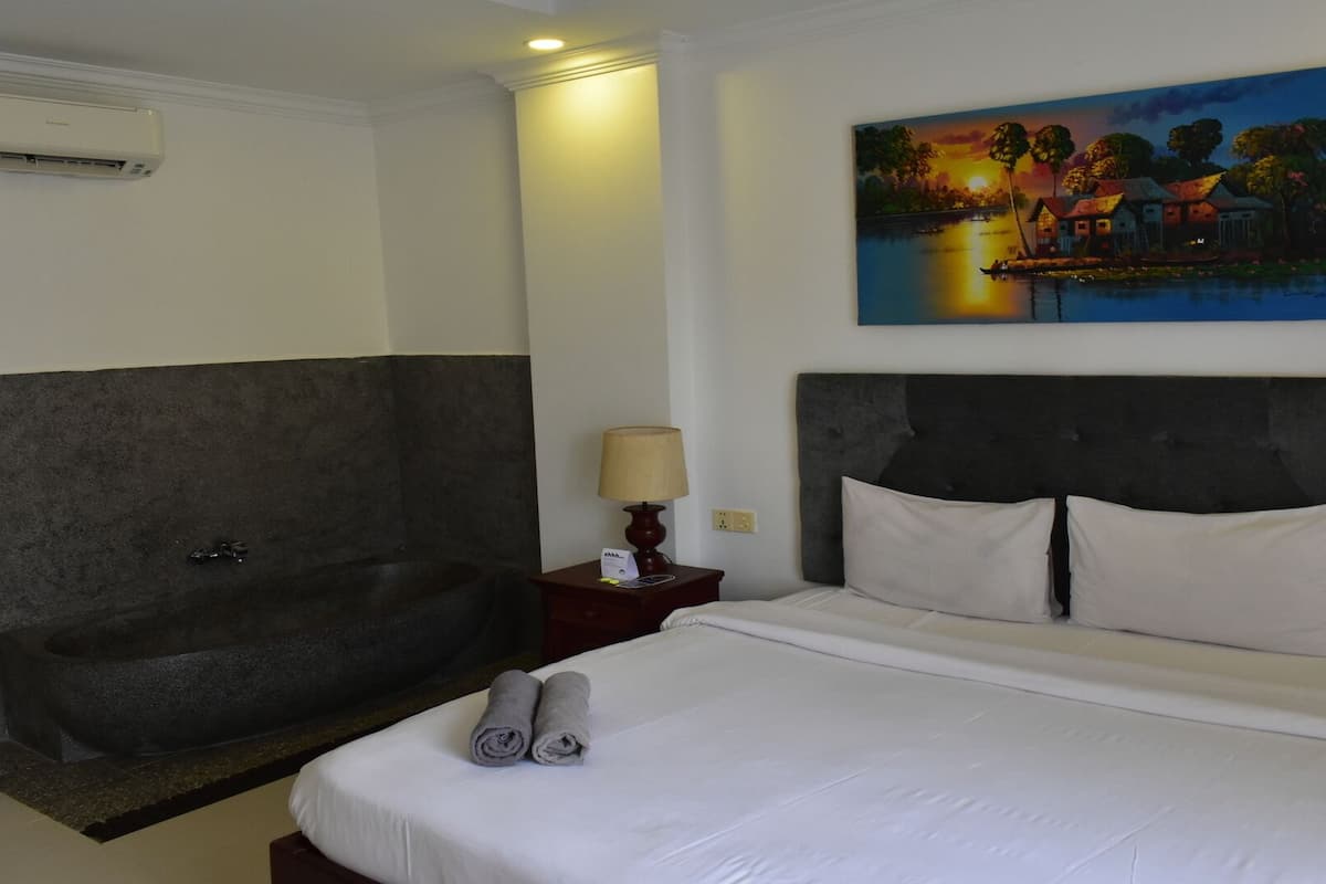 Habitación de hotel con una cama grande, una bañera y un cuadro de una escena de atardecer.