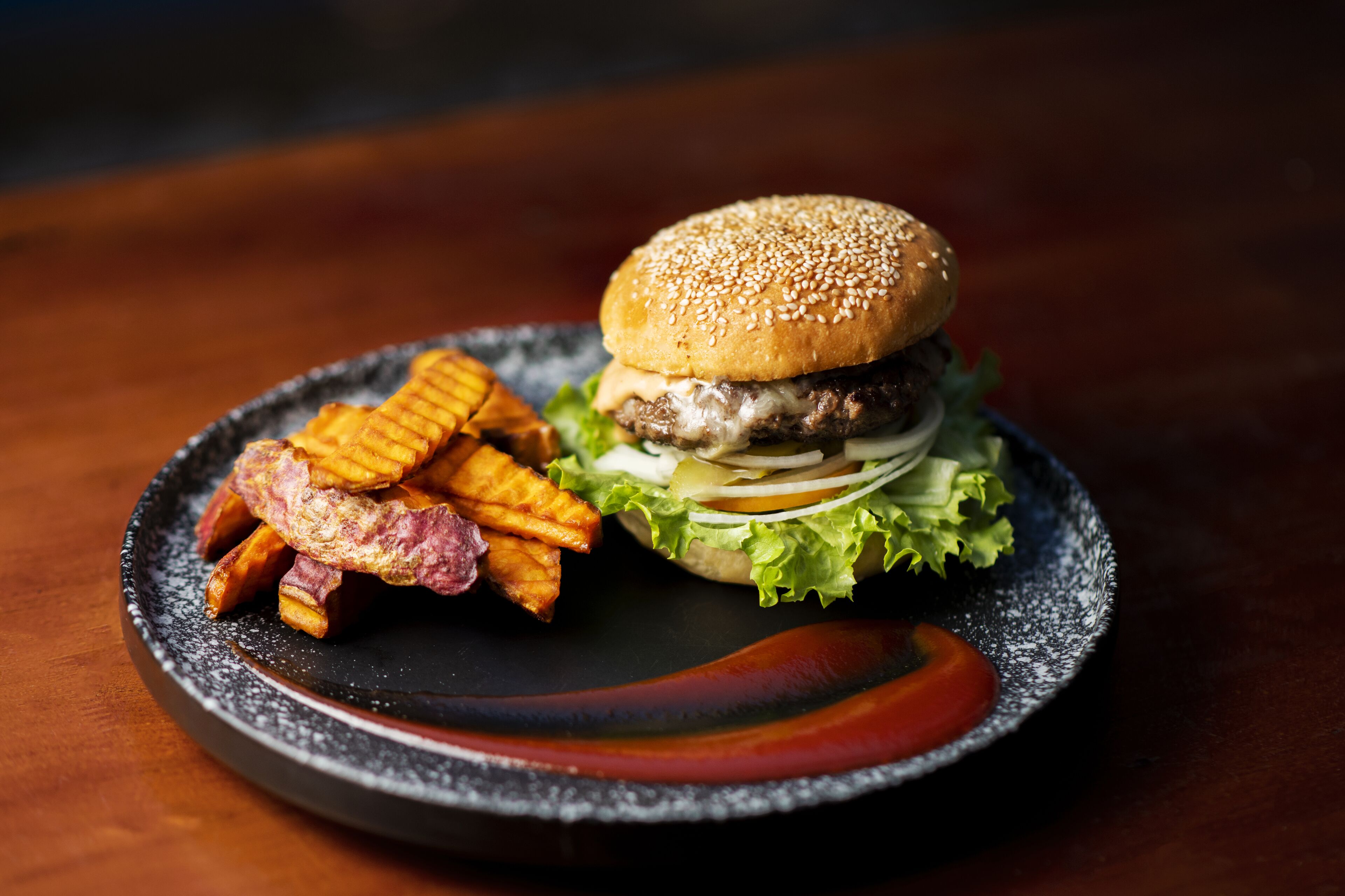 A plate with a burger, fries, and a slice of tomato on a dark plate.