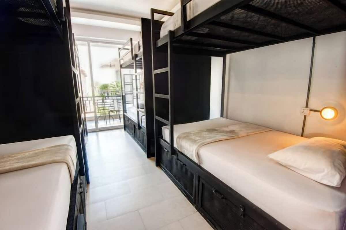 Une chambre avec un lit superposé, un matelas blanc, une table de chevet et un luminaire fixé au mur.