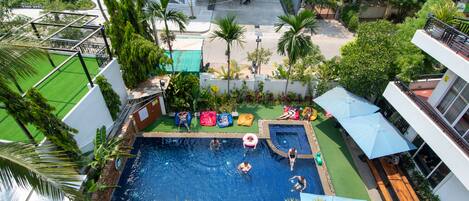 An outdoor swimming pool surrounded by greenery, with people swimming and lounging.