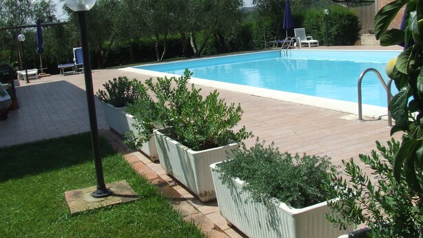 A swimming pool surrounded by a wooden deck, with potted plants and outdoor furniture. - Agriturismo Il Punto Verde (Campagnatico)