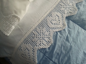 Una cama con sábana azul y encaje blanco en el borde.