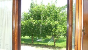 A view through a wooden-framed window with a white curtain, overlooking a grassy area with trees and a swing. - Agriturismo Il Punto Verde (Campagnatico)