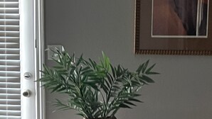 Une plante en pot est posée sur une petite table dans une pièce qui comporte une porte et un tableau encadré au mur.