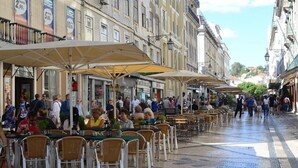 Café al aire libre con mesas y sillas, rodeado de edificios con grandes ventanales y balcones.