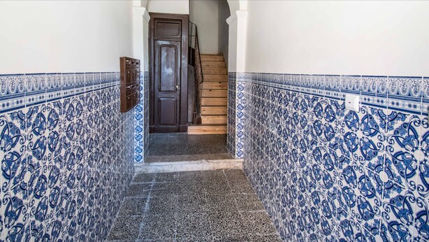 Un pasillo estrecho con baldosas de diseño azul y blanco, una puerta de madera y una escalera que sube a un nivel superior.