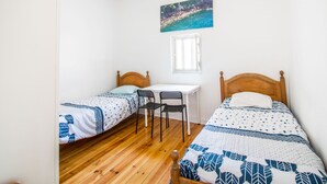Habitación con dos camas individuales, un escritorio pequeño, una silla y una ventana.