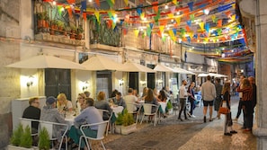Dine al fresco in a charming outdoor setting with tables and chairs nestled among cobblestone streets and lush greenery.