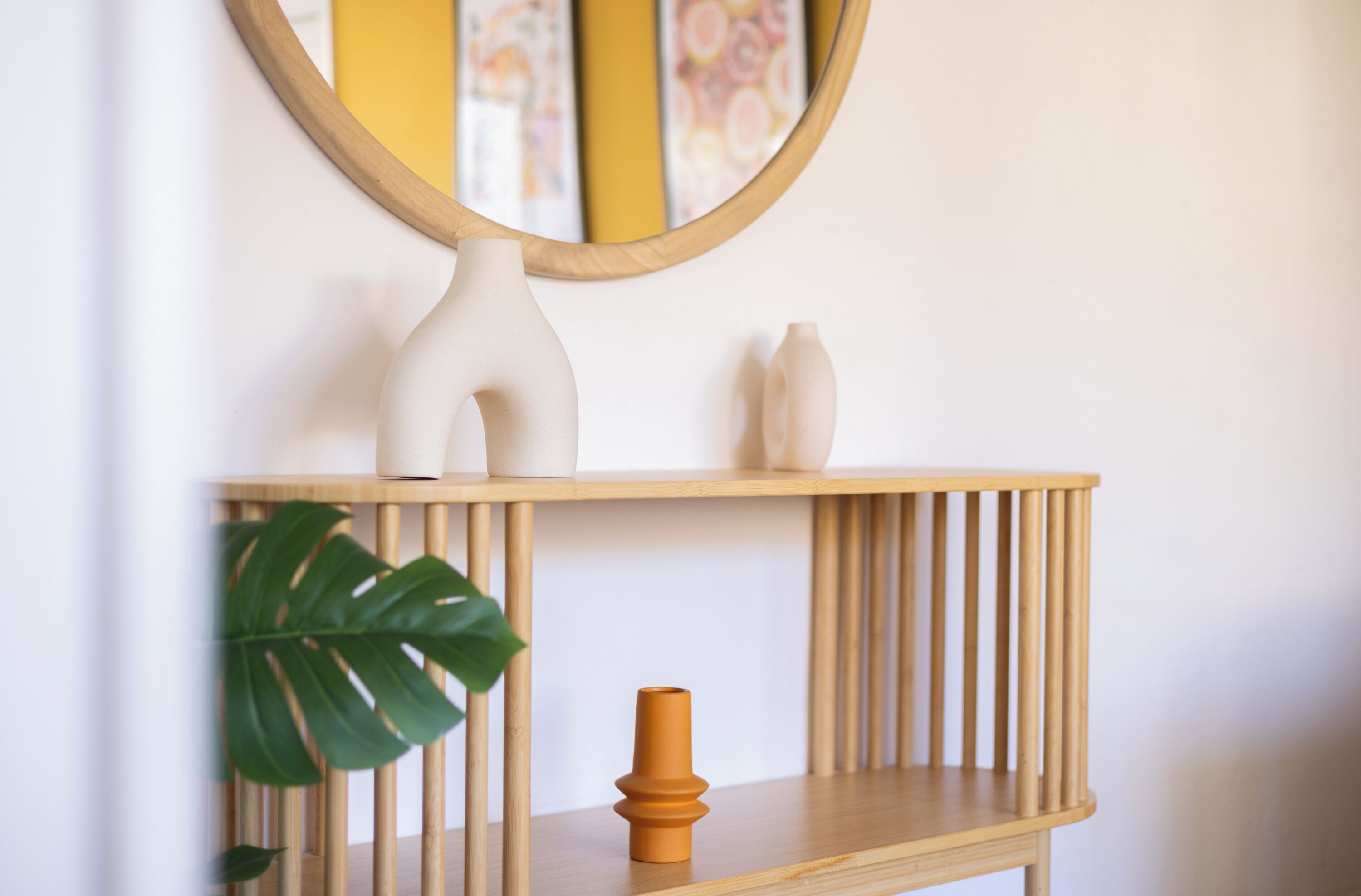 Une console en bois, avec un miroir au-dessus, une plante en pot et deux vases blancs.