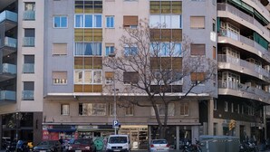 Monikerroksinen rakennus, jossa on parvekkeita, pysäköintikyltti ja puu sen edessä.