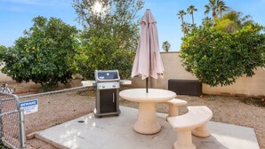 Een terras buiten met een barbecue, een tafel en banken.