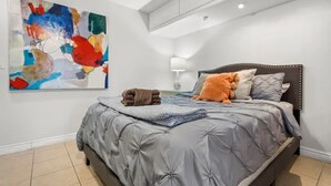 Een slaapkamer met een groot bed, een wanddecoratie in abstractie en een nachtkastje met een lamp.
