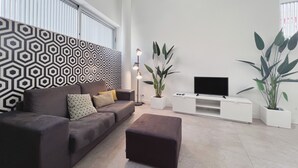 Una sala de estar moderna con una pared estampada, un sofá, un televisor de pantalla plana y plantas en macetas.