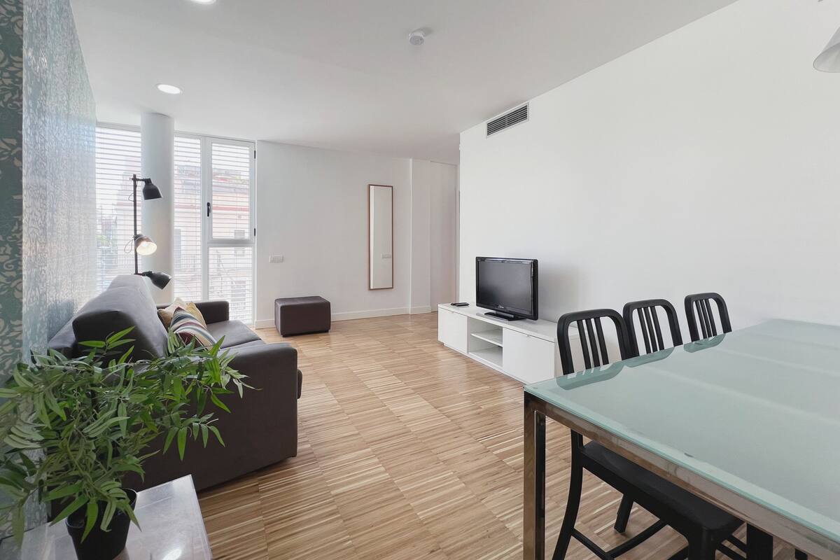 Una sala de estar moderna con un sofá, una mesa de comedor con sillas, un televisor y una planta en maceta.