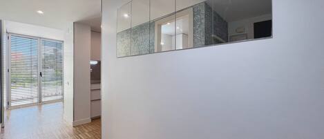 A hallway with a wooden floor, a sliding glass door, and a mirrored wall reflecting a kitchen area.