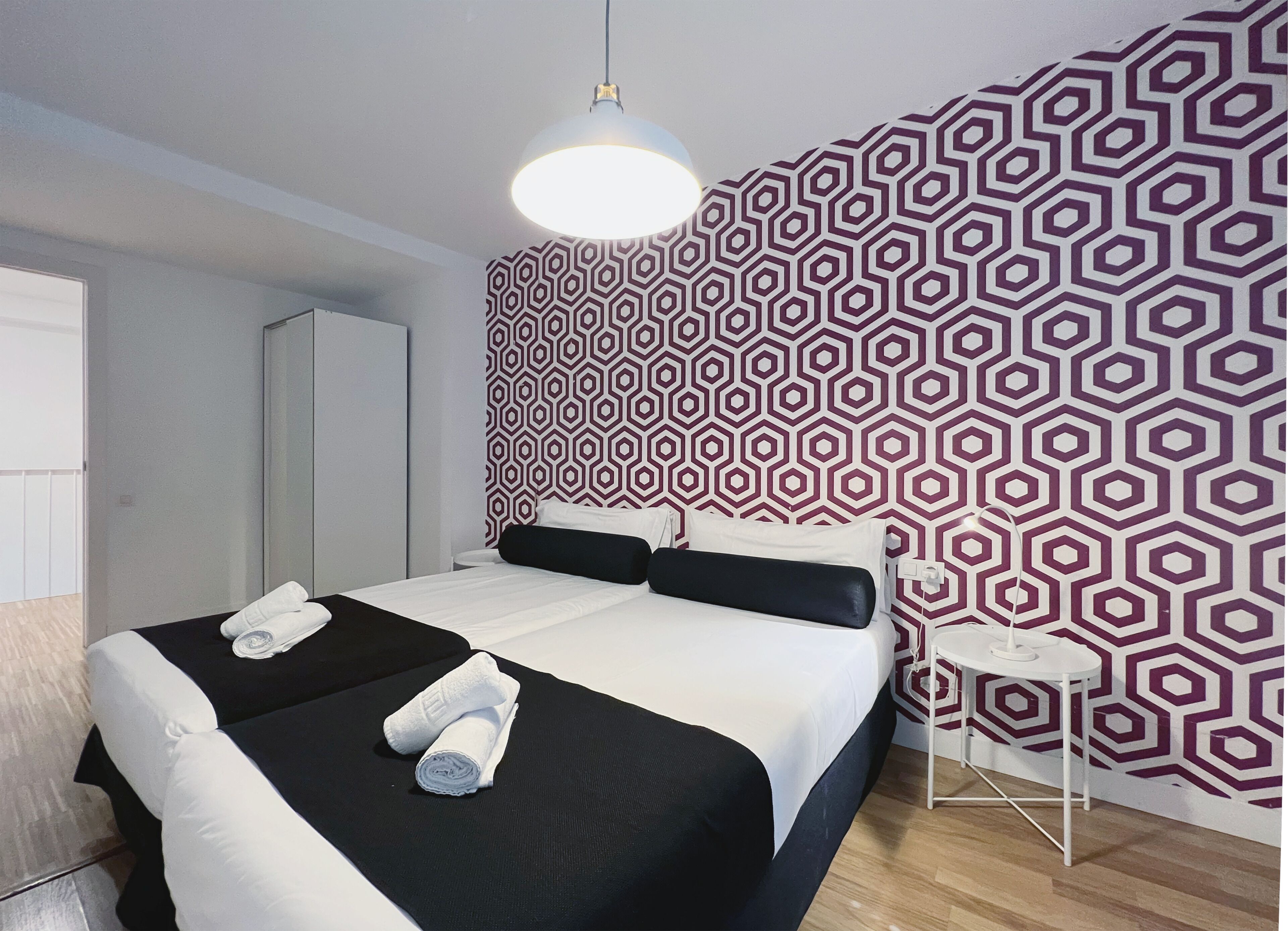 A modern hotel room with a large bed, a small side table, and a geometric patterned wall.