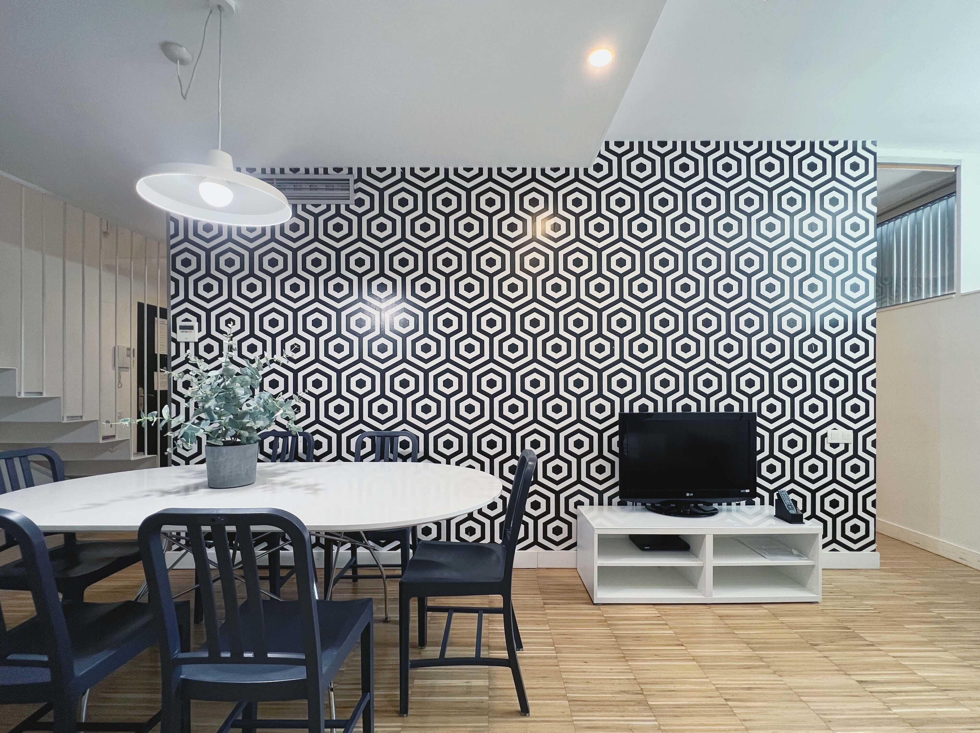 Un comedor moderno con una pared de diseño geométrico, una mesa redonda y sillas negras.