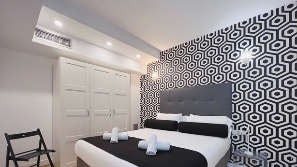 Habitación de hotel moderna con una cama, un armario, una silla y un papel tapiz estampado.