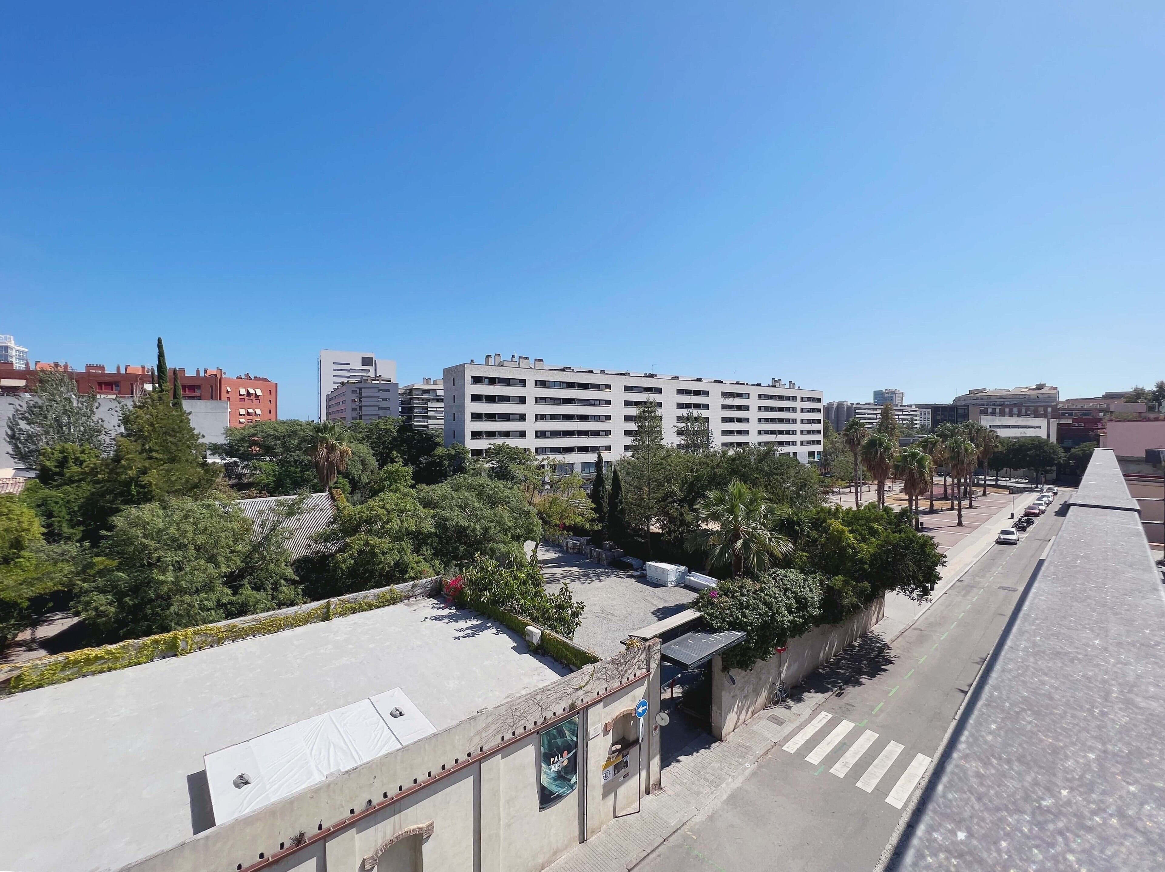 Un edificio de varios pisos con techo plano, rodeado de árboles y un cielo despejado.