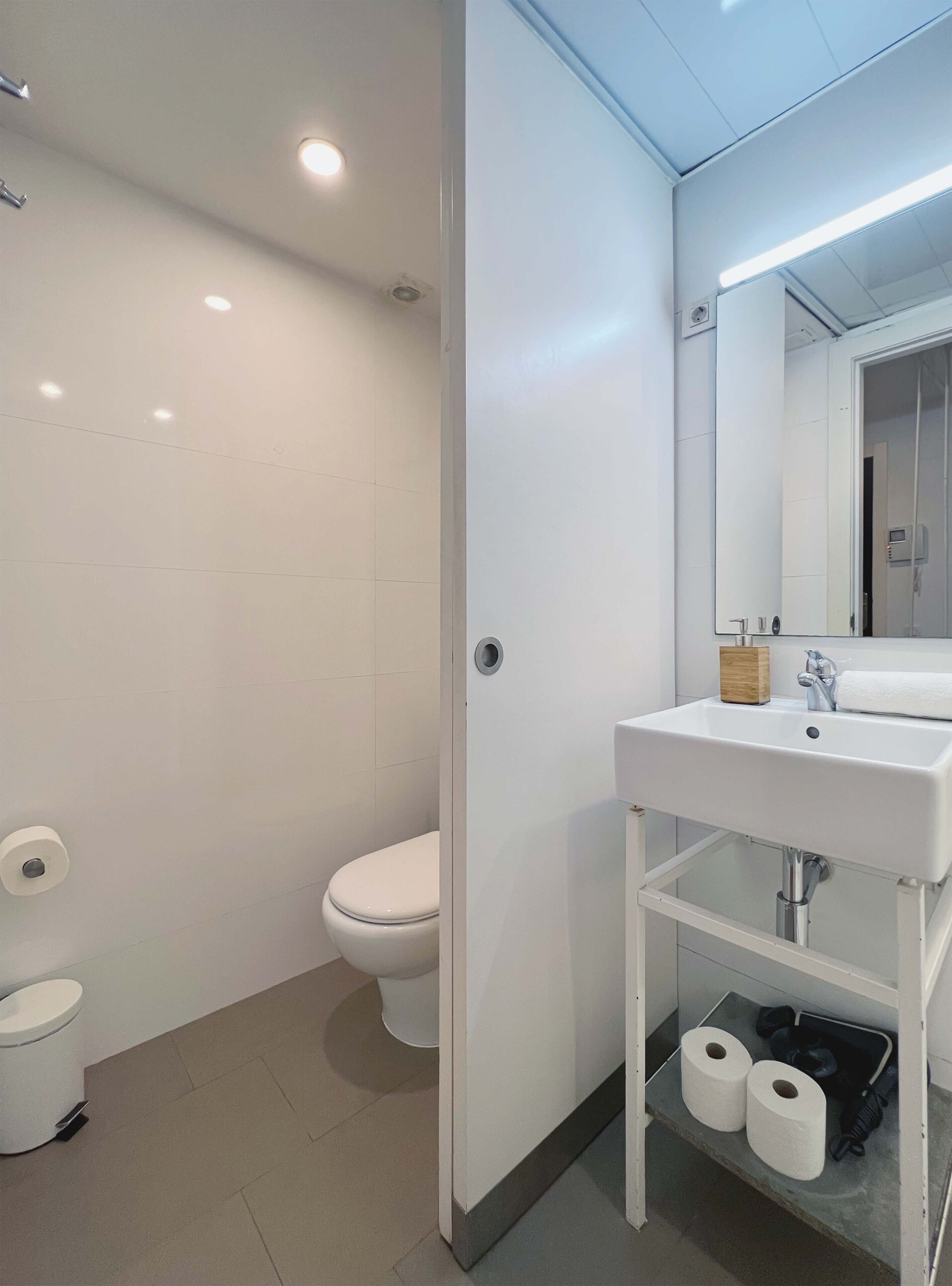 A modern bathroom with a white toilet, a sink with a mirror, and two rolls of toilet paper on the floor.