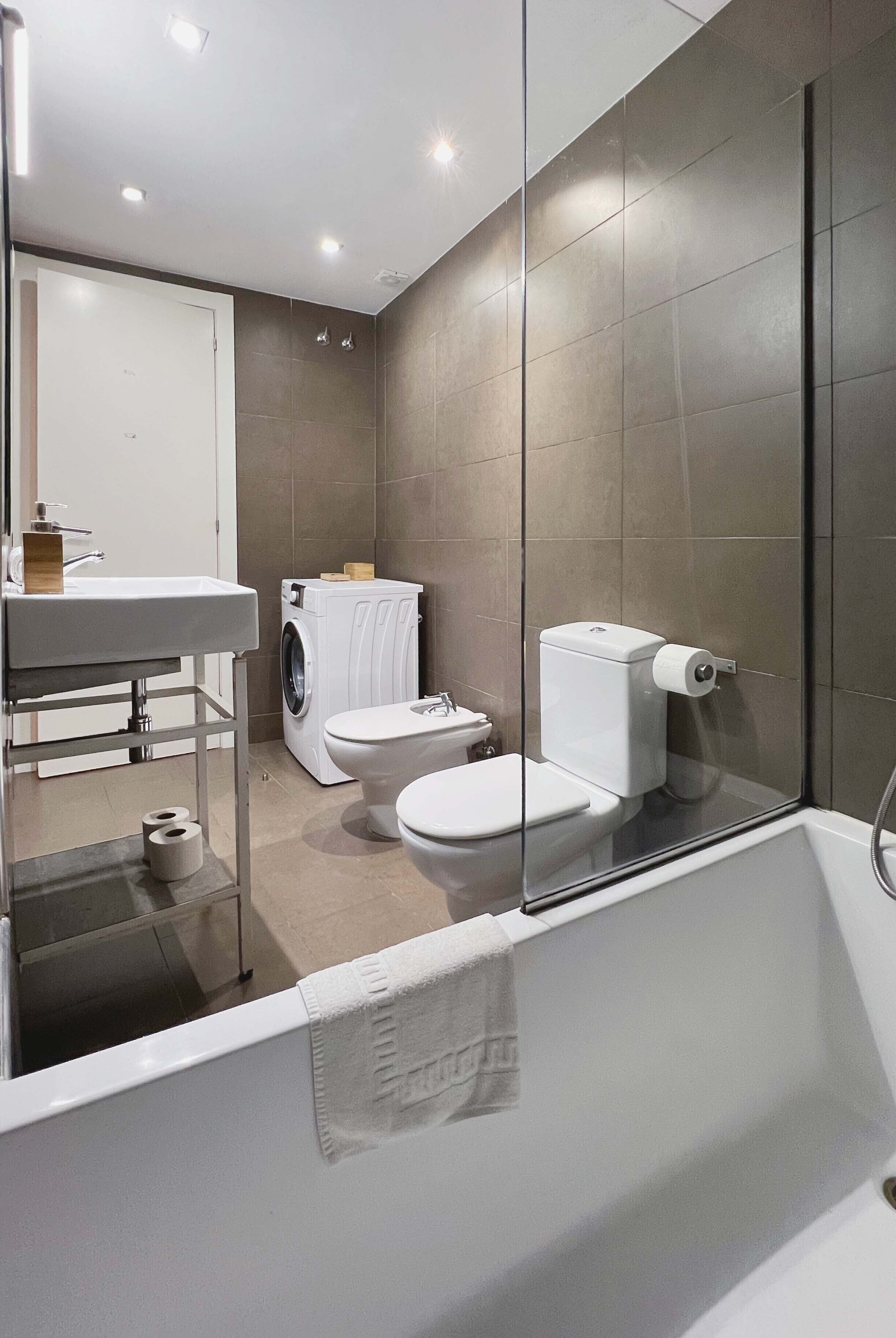 Une salle de bain moderne avec une douche à parois de verre, un lavabo blanc, des toilettes et un lave-linge.