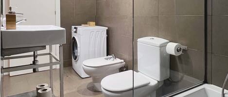 Une salle de bain moderne avec une douche à parois de verre, un lavabo blanc, des toilettes et un lave-linge.