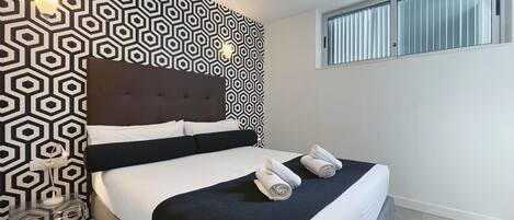 Una habitación de hotel moderna con una pared de diseño geométrico, una cama grande con ropa blanca y dos toallas enrolladas sobre la cama.