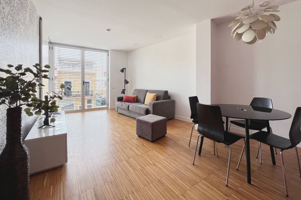 Una sala de estar moderna con un sofá gris, sillas negras, una mesa de comedor y una lámpara colgante.