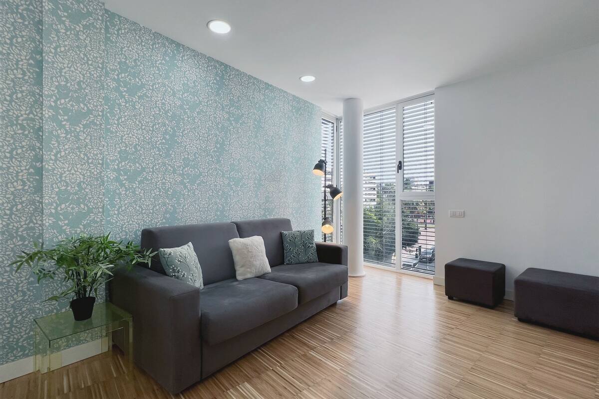 Una sala de estar moderna con un sofá gris, una mesa de centro de vidrio y una planta en maceta.