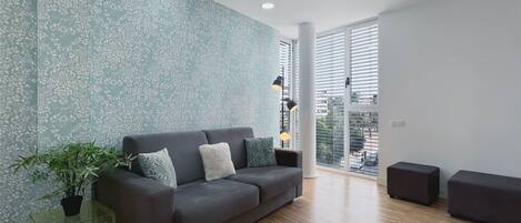 A modern living room with a grey sofa, a glass coffee table, and a potted plant.