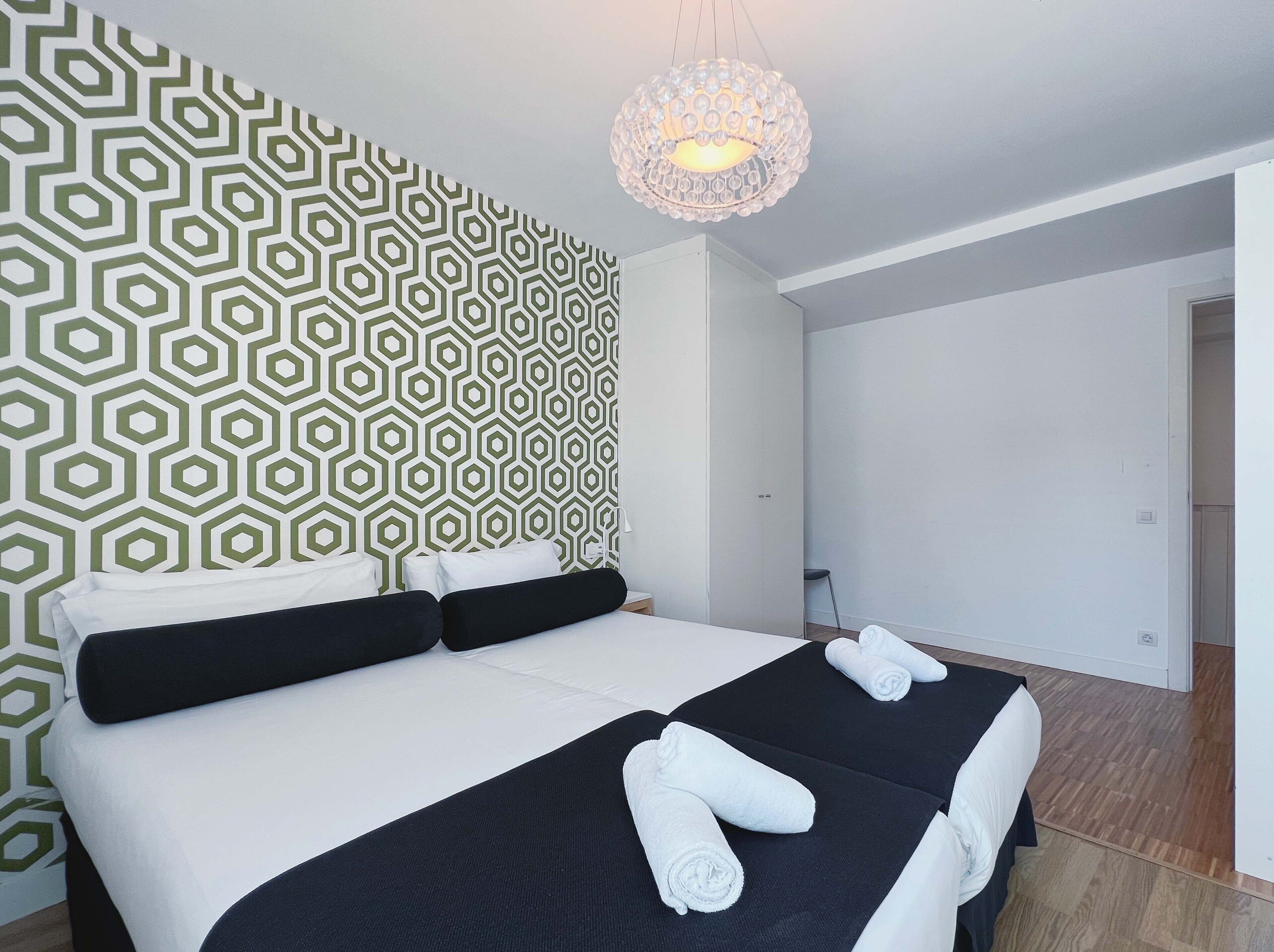 A hotel room with a geometric patterned wall, a large bed with white and black bedding, and a chandelier.