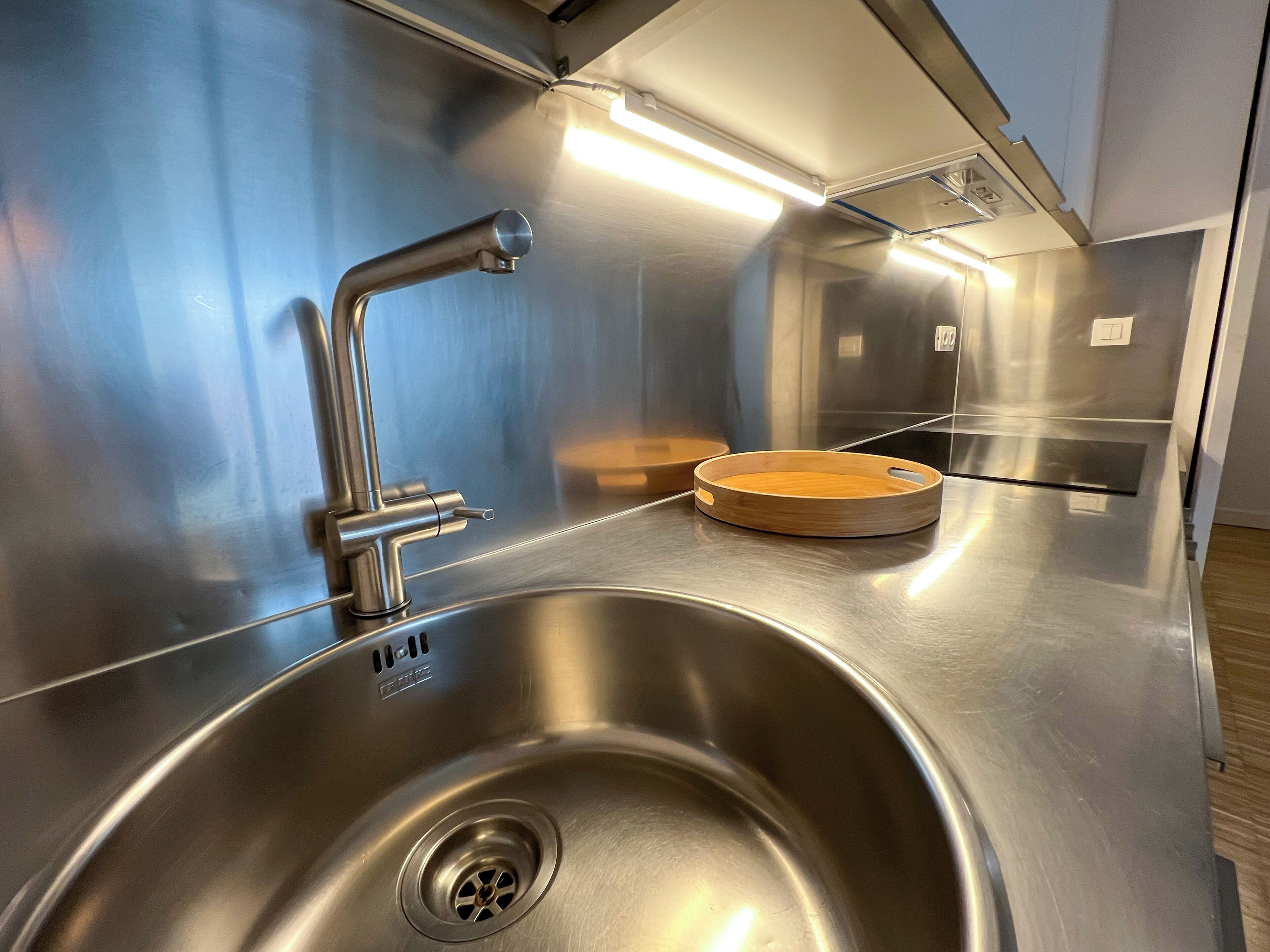 A stainless steel sink with a modern faucet, a wooden tray, and a built-in light above the sink.